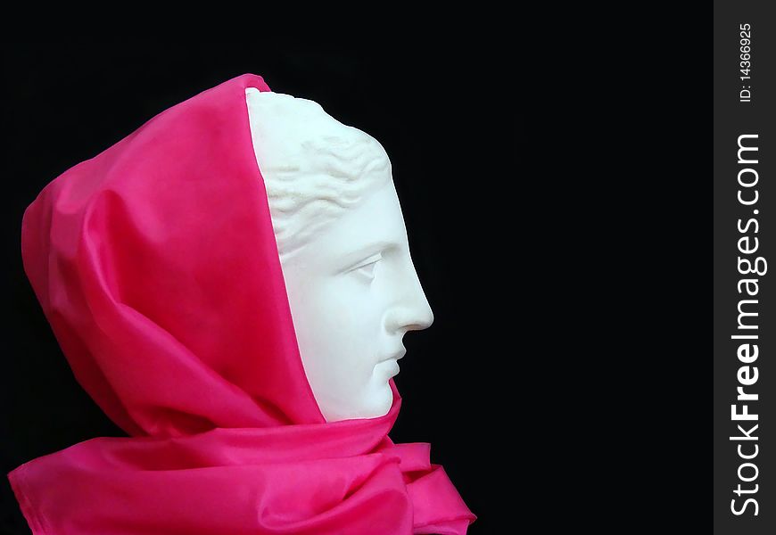 Plaster head of Venus in  a pink scarf on a black background. Plaster head of Venus in  a pink scarf on a black background