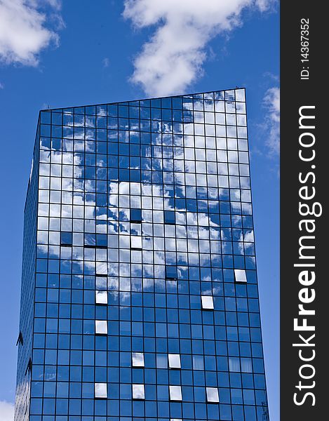 Glass tower with blue sky with clouds reflecting in the glass.