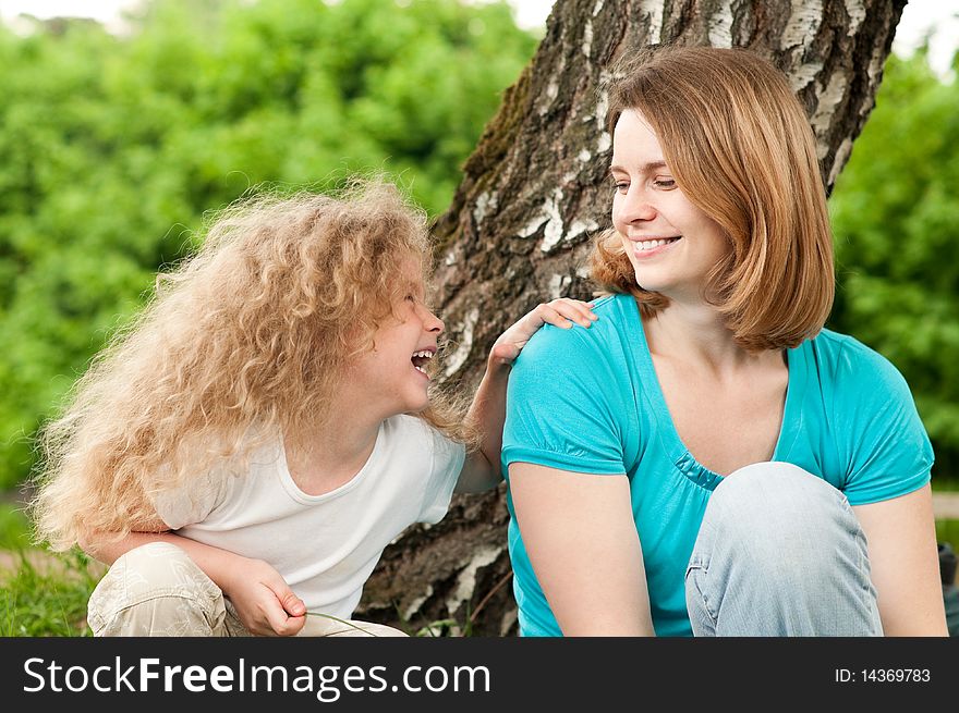 Happy young mother sitting in park with her beautiful laughing daughter. Happy young mother sitting in park with her beautiful laughing daughter