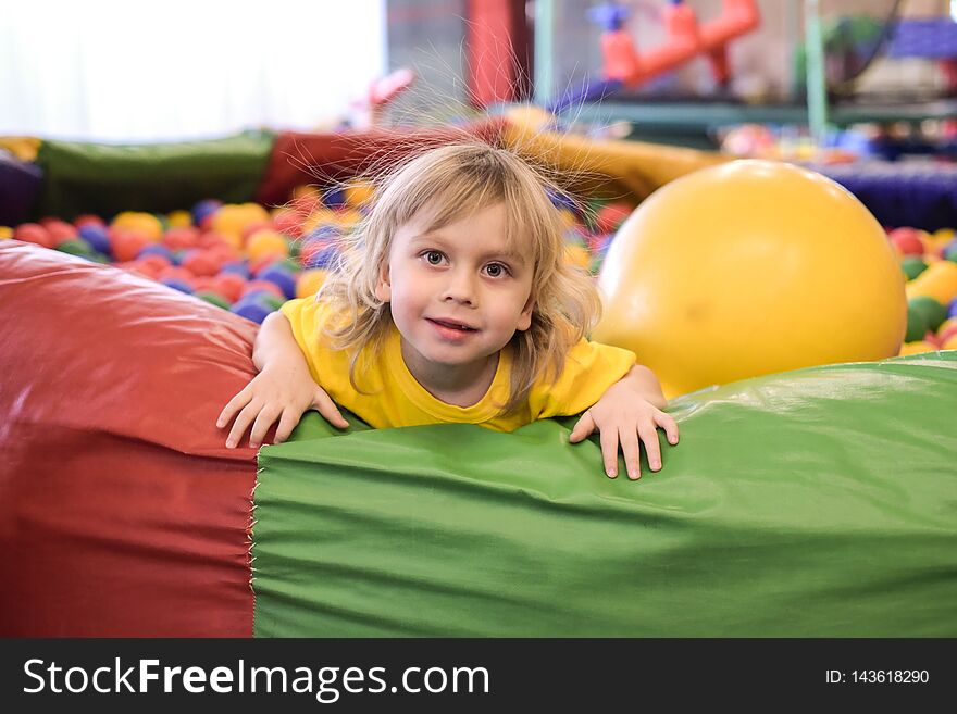 Portrait of a blond boy in a yellow t-shirt. The child smiles and plays in the children`s playroom. Ball pool.