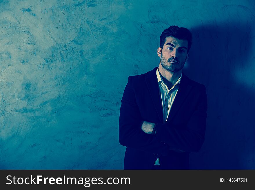 A serious handsome young businessman in a black suit standing in front of a grey wall in a studio. A serious handsome young businessman in a black suit standing in front of a grey wall in a studio.