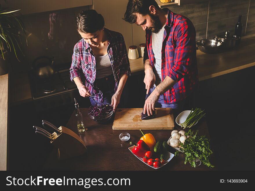 Beautiful young couple in kitchen at home while cooking healthy food. Husband cut cabbage. Wife mix salad. Scene from family life. Horizontally framed shot