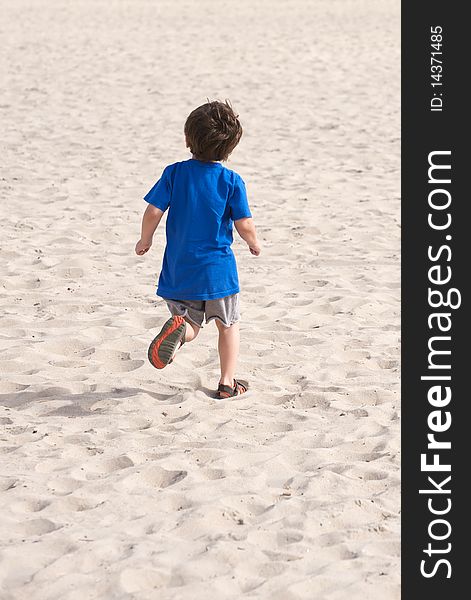 Latino boy running on the beach. He's getting away from the camera wearing a blue t-shirt. Latino boy running on the beach. He's getting away from the camera wearing a blue t-shirt