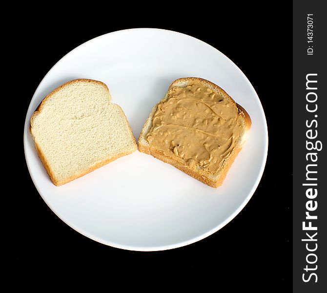 An open crunchy peanut butter sandwich made with white bread is on a white plate with black background
