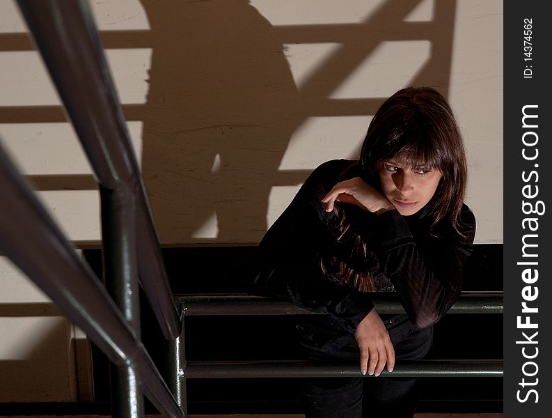 A portrait of a young woman waiting in a stairwell with shadows behind her. A portrait of a young woman waiting in a stairwell with shadows behind her