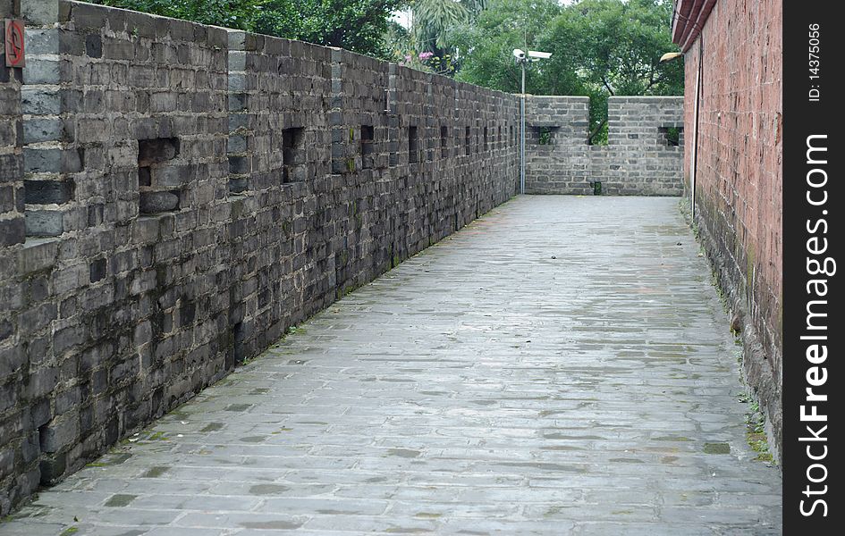 This shot is of stone side walk with walls on either side. The wall on the right is grey, the wall on the left is red. A set of security cameras can be seen in the back side of the image. This shot is of stone side walk with walls on either side. The wall on the right is grey, the wall on the left is red. A set of security cameras can be seen in the back side of the image.