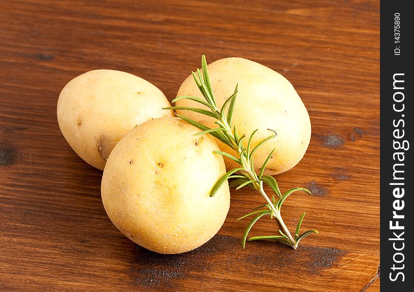 Photo of three potatoes which are unpeeled and standing on a wood table