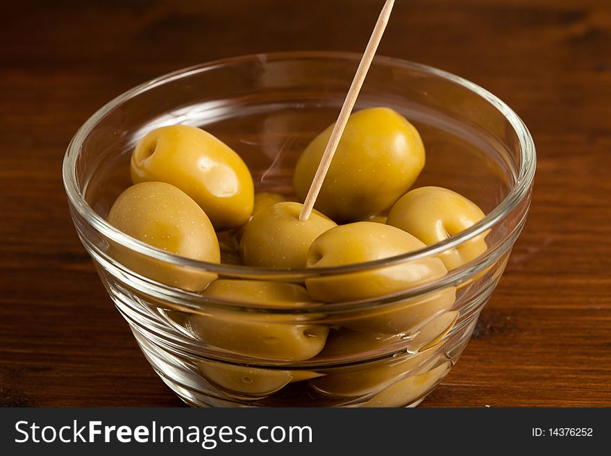 Photo of green olives in a bowl standing on a wood table