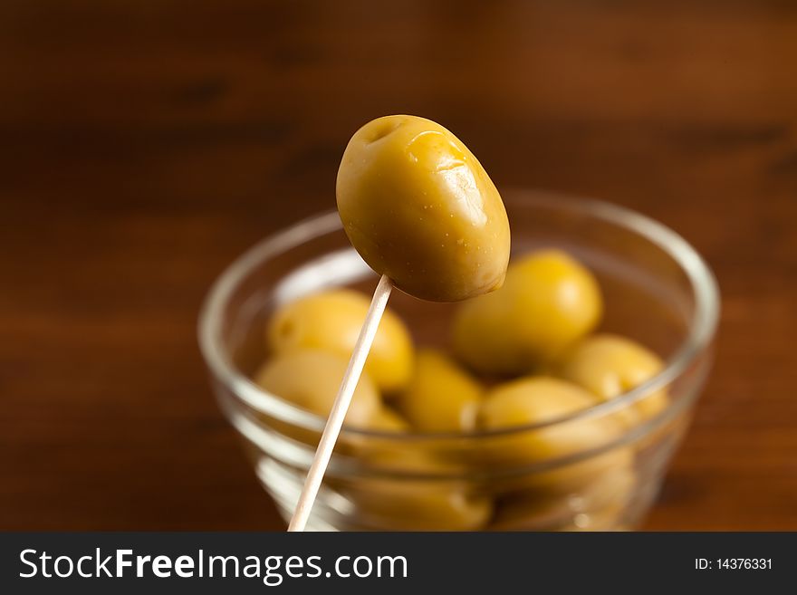 Photo of green olives in a bowl standing on a wood table