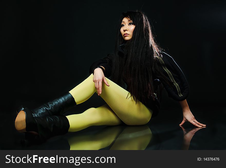 Sitting brunette asian model on black background with night reflections