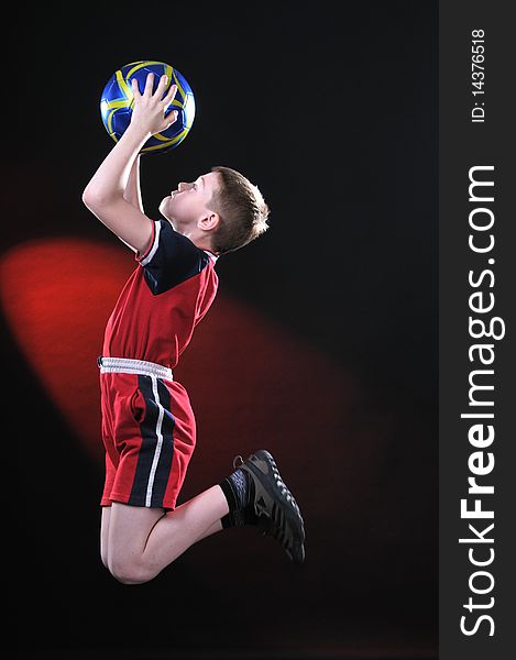 Boy ten years in a jump on a dark background and catches a soccer ball. Boy ten years in a jump on a dark background and catches a soccer ball