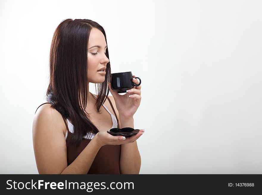 Beautiful young brunette drinking coffee in the studio with rear blym background