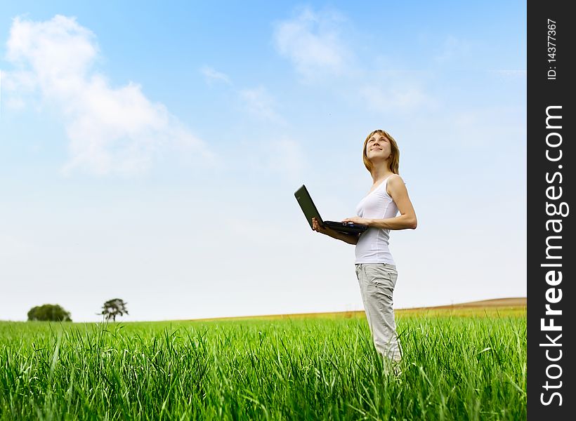 Young smiling woman with laptop standing on meadow with green grass