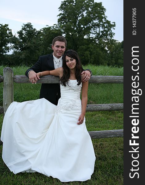 Attractive married couple standing together looking at  camera leaning against fence. Attractive married couple standing together looking at  camera leaning against fence