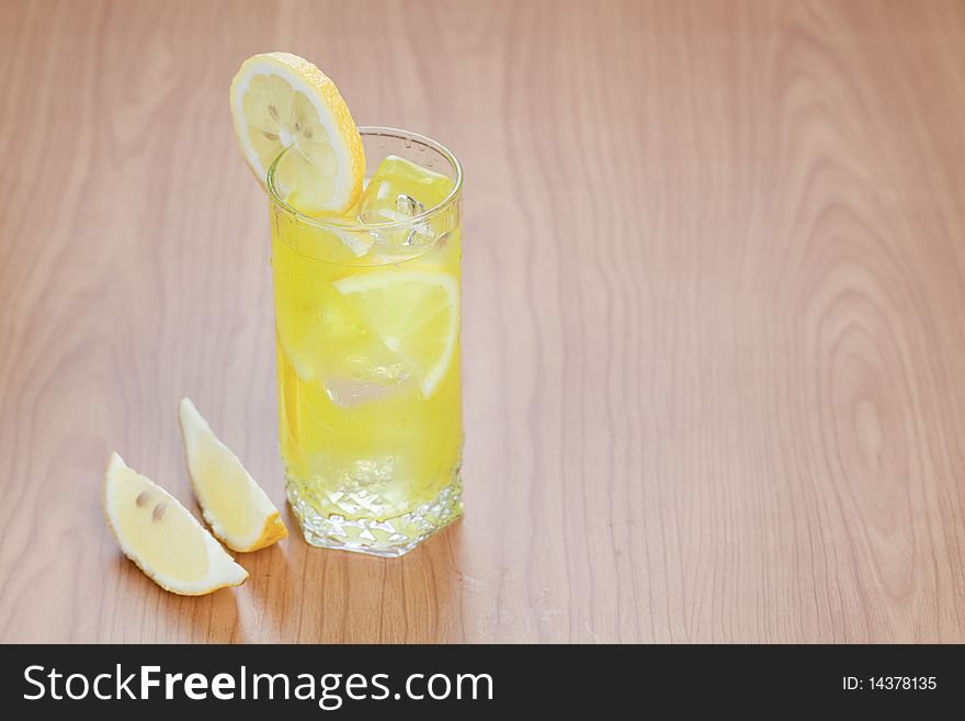Glass of cold lemon beverage on wooden table top with space for text