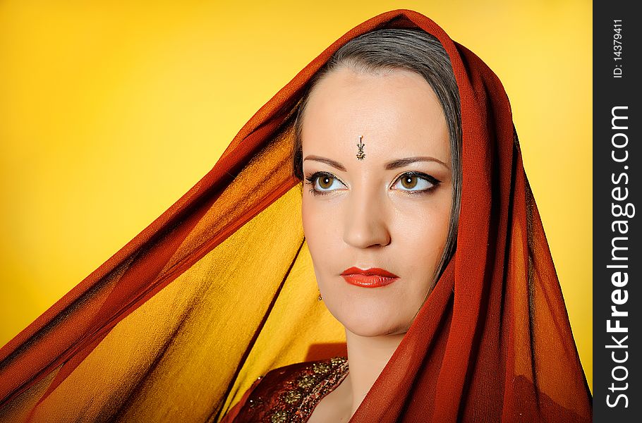 Young beautiful woman in indian traditional jewellery, bindi and make-up. yellow background. Young beautiful woman in indian traditional jewellery, bindi and make-up. yellow background