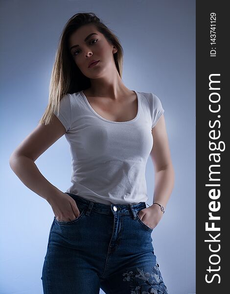 Low key girl portrait with blonde hair in white t shirt and blue jeans, looking on camera and hands in pockets. Female portrait in studio Close up. Low key girl portrait with blonde hair in white t shirt and blue jeans, looking on camera and hands in pockets. Female portrait in studio Close up