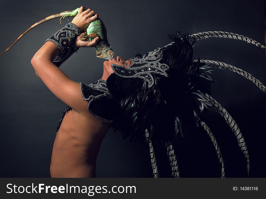 Young pagan priest in ritual suit with green iguana in his hands. Photo.