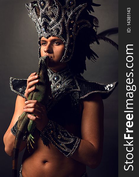 Young pagan priest in ritual suit with green iguana in his hands. Photo.