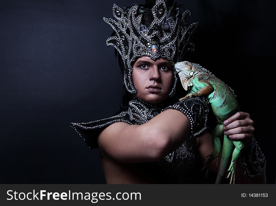 Young pagan priest in ritual suit with green iguana in his hands. Photo.