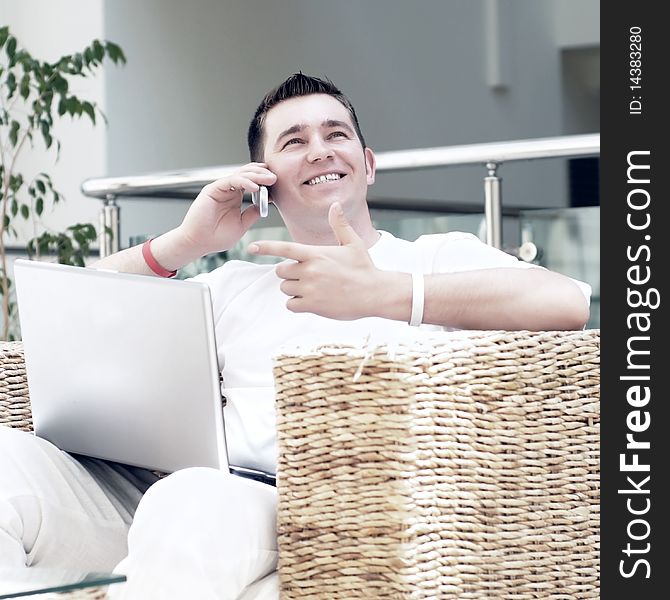 Smiling young man working on laptop computer and call by phone at home