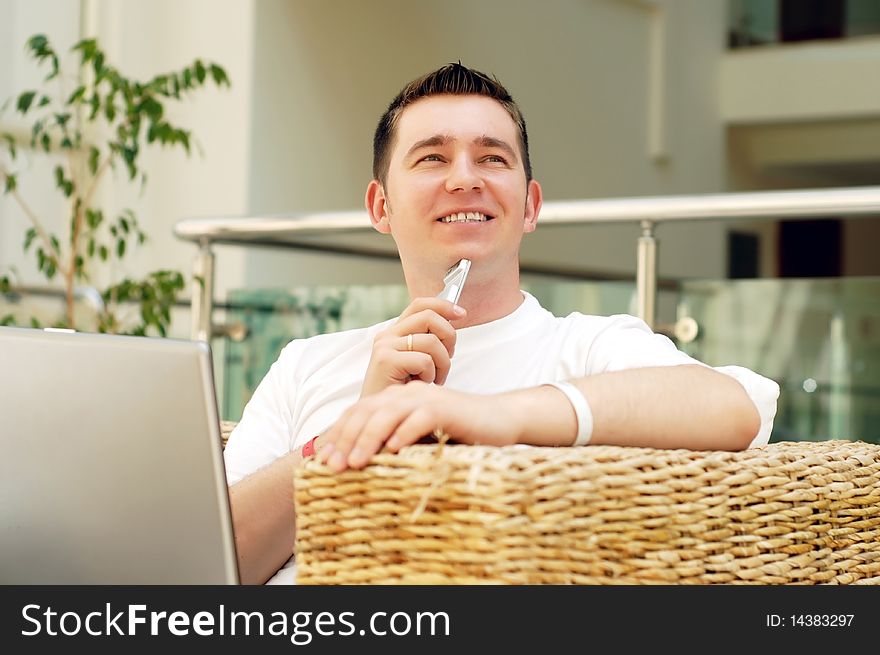 Smiling young man working on laptop computer and call by phone at home