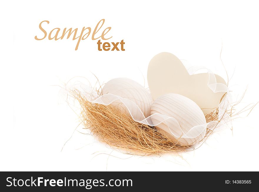 Decorative eggs lying on some hay with white ribbon and heart isolated on white