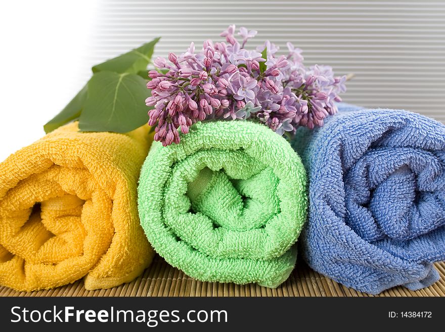 Colored towels folded lie next to them a branch of lilac. Colored towels folded lie next to them a branch of lilac