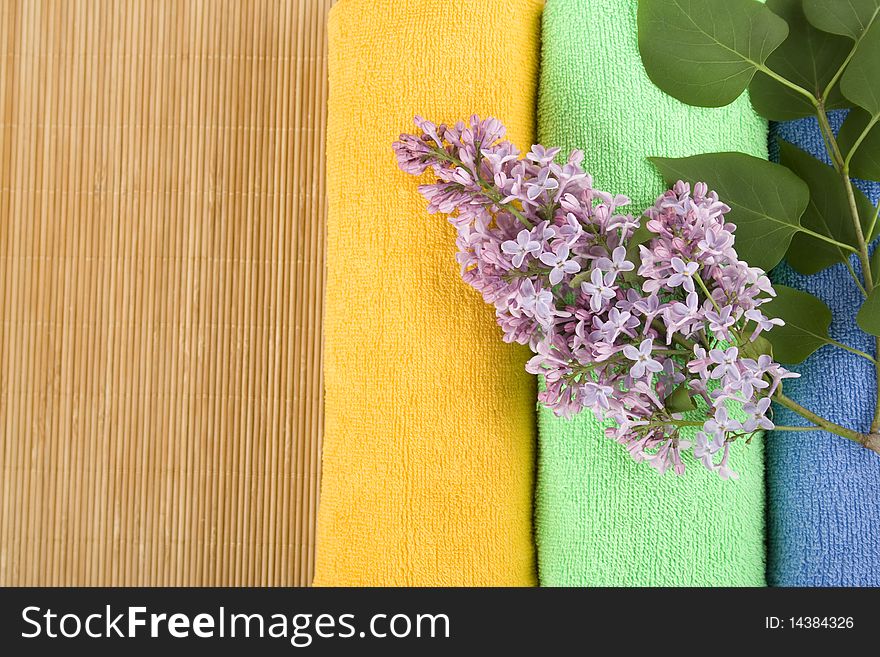 Colored towels folded lie next to them a branch of lilac. Colored towels folded lie next to them a branch of lilac