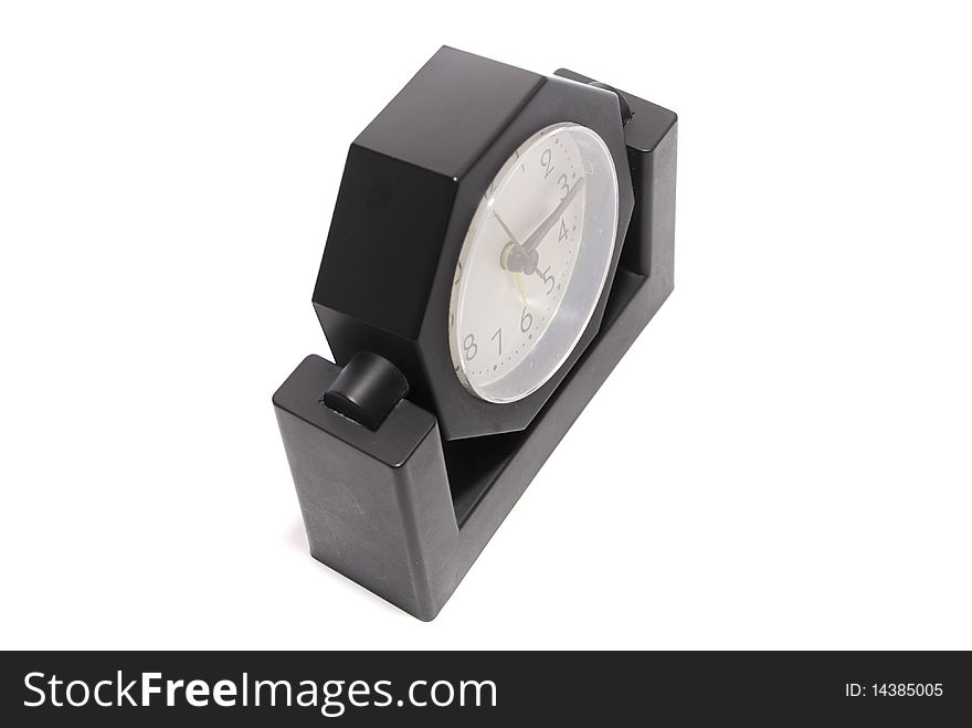 Black alarm clock with white analog dial, a rotating body hexagon shape on a white background, top view. Black alarm clock with white analog dial, a rotating body hexagon shape on a white background, top view