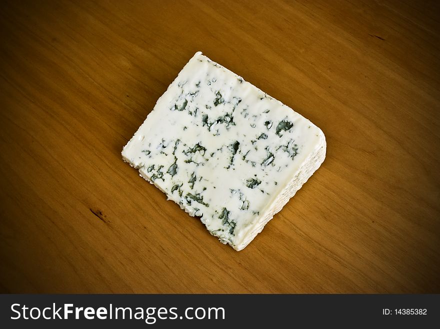 A slice of creamy blue cheese on a wooden board. A slice of creamy blue cheese on a wooden board