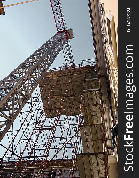 Crane and construction scaffold near a building under restructuring. Crane and construction scaffold near a building under restructuring