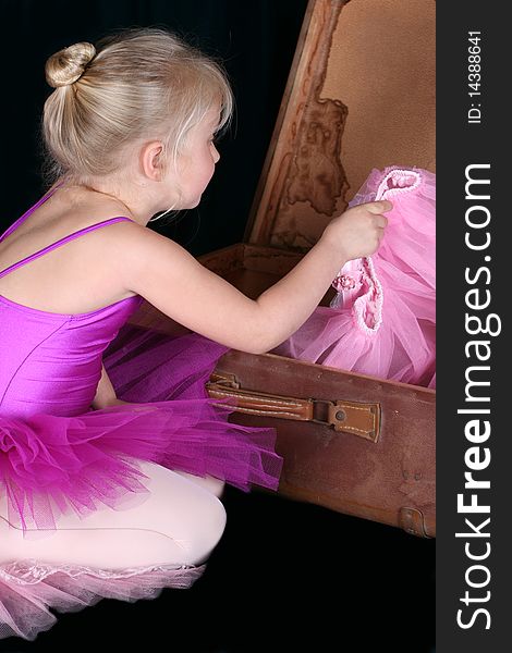 Little blond ballerina looking for a costume in an antique suitcase