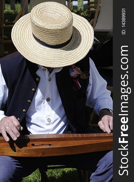 Man in a straw hat plays a dulcimer at a Civil War festival. Vertical shot. Man in a straw hat plays a dulcimer at a Civil War festival. Vertical shot