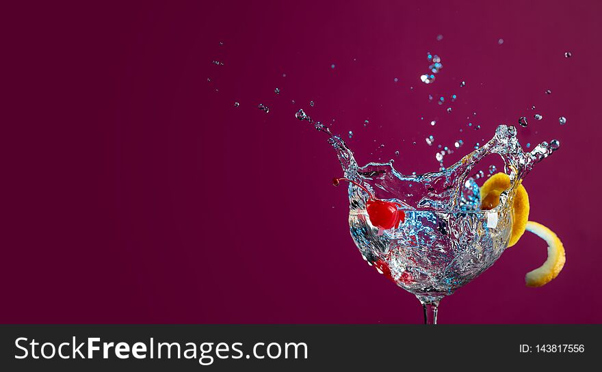 Colorful cocktail in glass with splashes garnished with lemon and cherries. Purple background. Mixed light. Copy space for your text