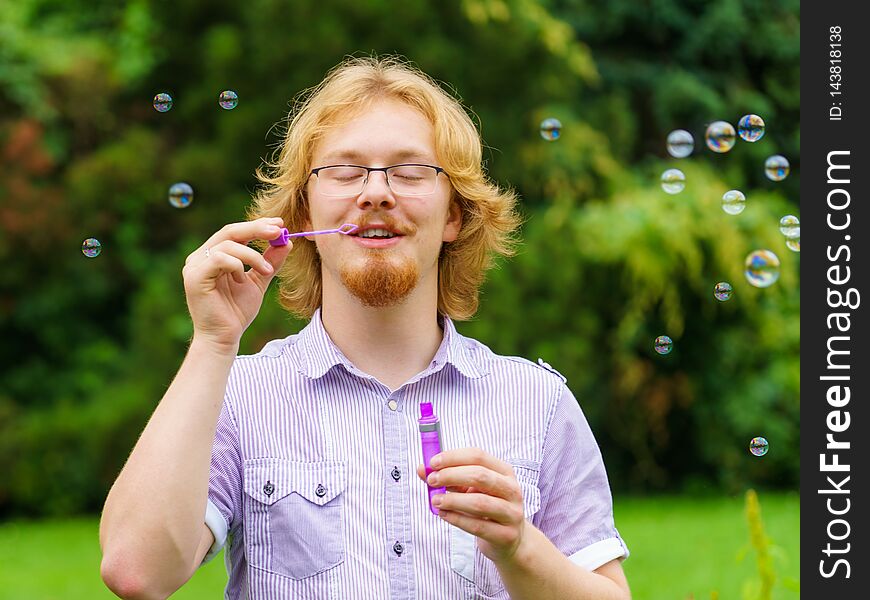 Happiness and carefree concept. Young man having fun blowing soap bubbles outdoor in park. Happiness and carefree concept. Young man having fun blowing soap bubbles outdoor in park