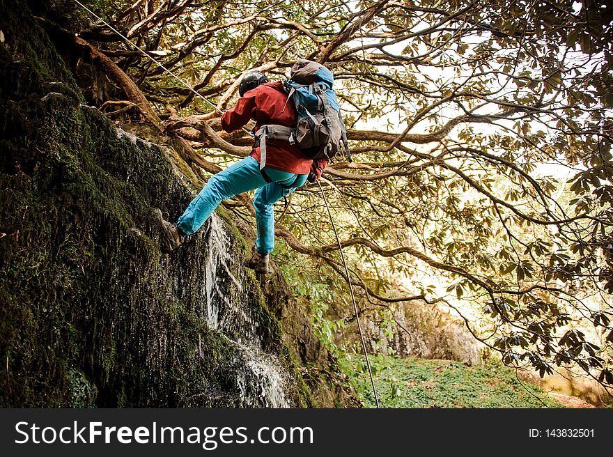 Young man in a red jacket with backpack dulfers down the mountains with trees and small beautiful waterfall in Adjara. Young man in a red jacket with backpack dulfers down the mountains with trees and small beautiful waterfall in Adjara