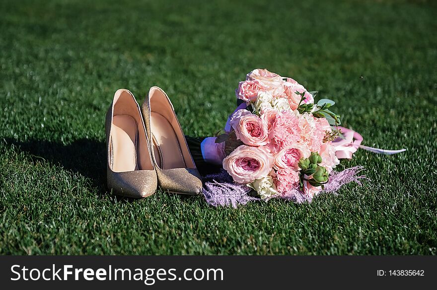 Luxury wedding bouquet with pink carnations and brilliant shoes. Accessories of the bride lie on a green lawn. Luxury wedding bouquet with pink carnations and brilliant shoes. Accessories of the bride lie on a green lawn
