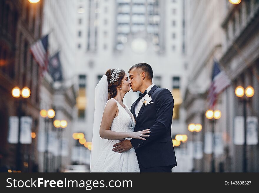 Elegant bride in a white dress and veil. Handsome groom in a blue suit. Couple in a big city. Elegant bride in a white dress and veil. Handsome groom in a blue suit. Couple in a big city