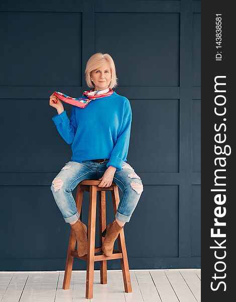 Senior model. Woman beauty. Attractive aged lady sitting on bar stool. Elegance and confidence. Trendy blue outfit. Senior model. Woman beauty. Attractive aged lady sitting on bar stool. Elegance and confidence. Trendy blue outfit.