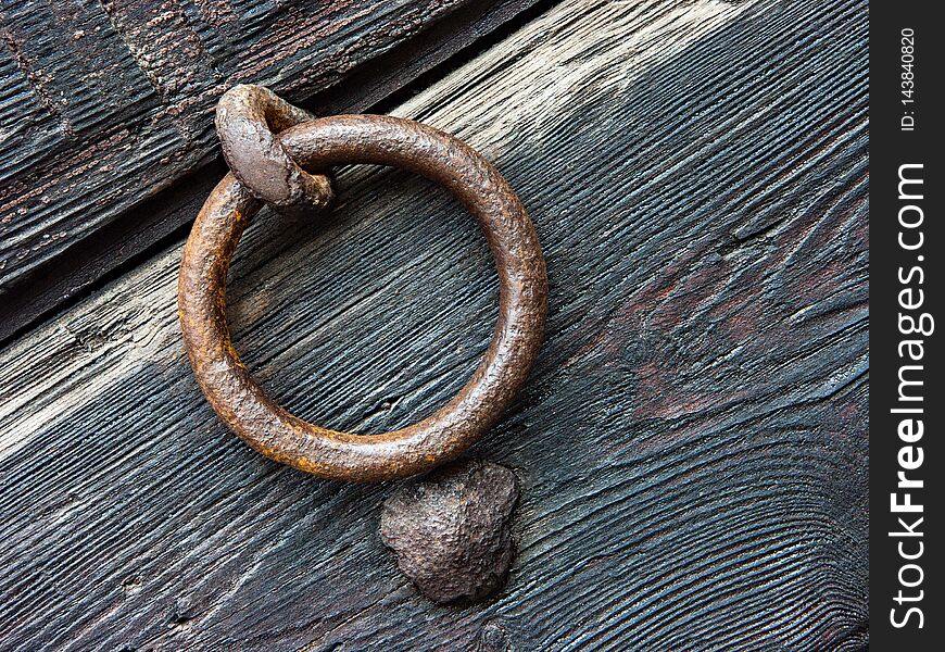 Door knocker with rust of ancient door in eroded wood. Rural house in Italy, province of Modena.