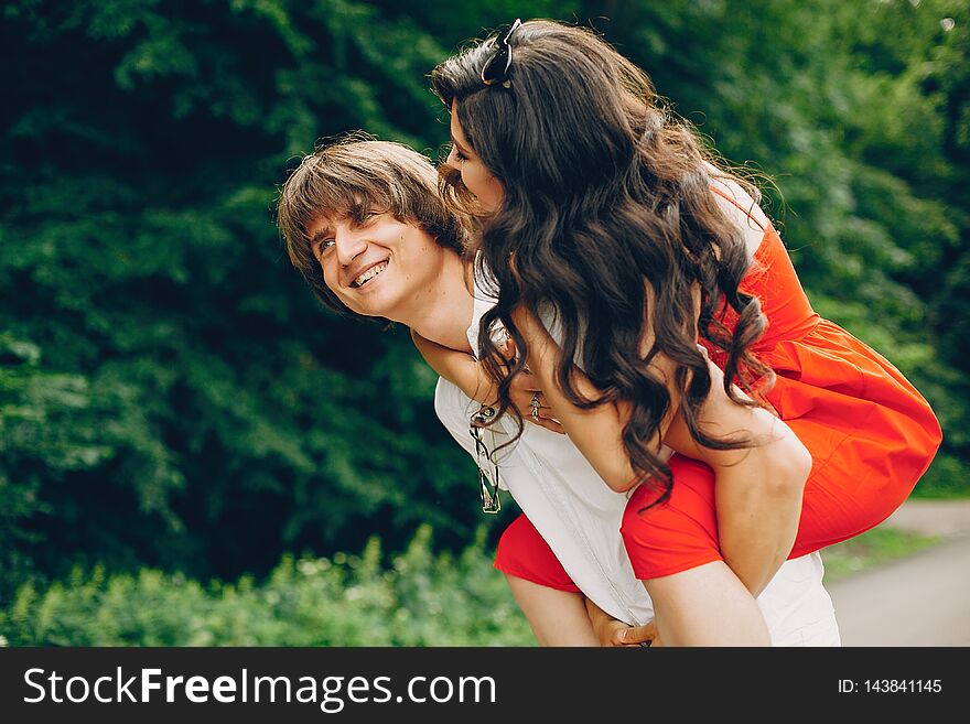 Pretty brunette with her boyfriend. Couple in a summer park. Lady in a red dress. Pretty brunette with her boyfriend. Couple in a summer park. Lady in a red dress