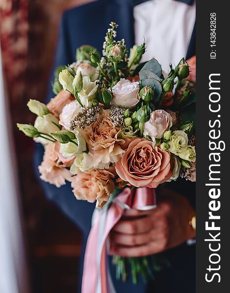 The groom holds elegant wedding bouquet in his hands