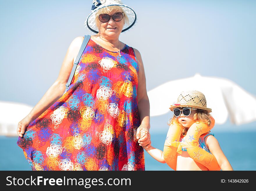 Adorable little girl wearing sunglasses, inflatable over-sleeves floats and inflatable donut float ring standing at the beach with