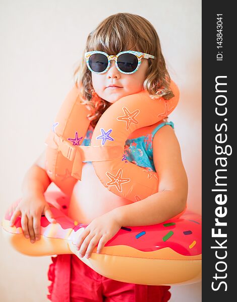 Adorable little girl ready to go for the beach, wearing sunglasses, inflatable over-sleeves floats and inflatable donut float ring. Safety in the water concept.