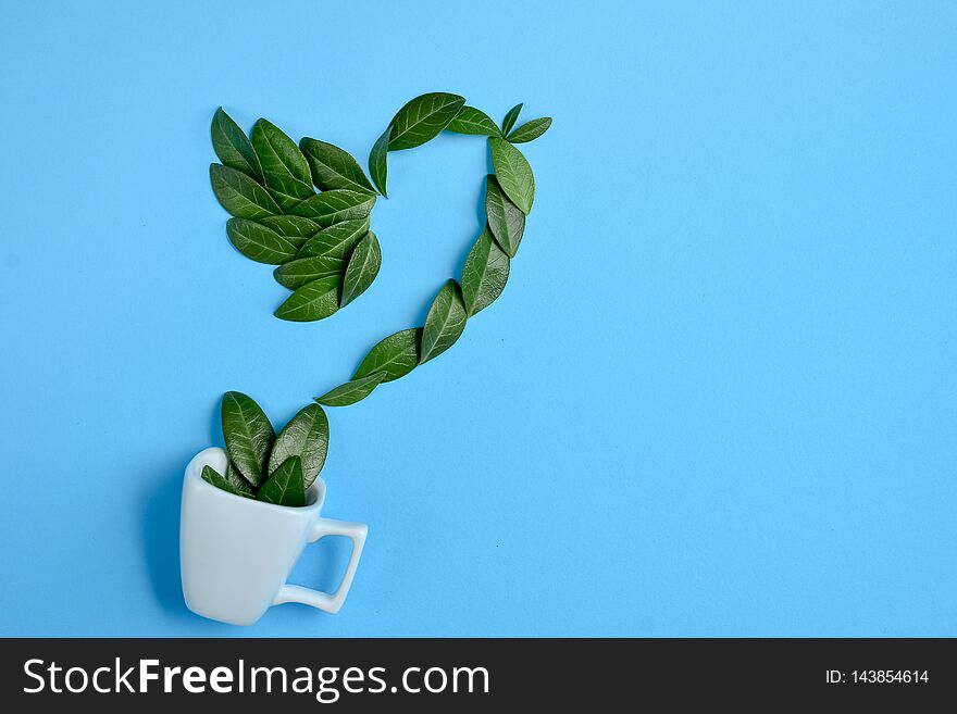 Coffee cup with bird made of natural green leaves on blue background. Flat lay, top view, copy space.