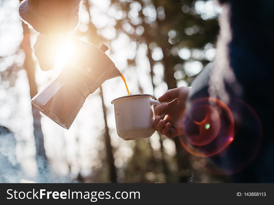 Outdoor shot of young woman pours itself hot beverage in mountains near to bonfire during the sunset. Traveler girl sitting and holding a mug of coffee after hiking. Adventure and camping concept