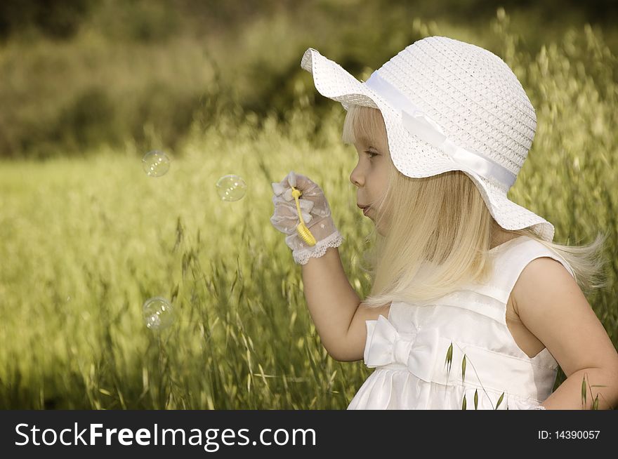 Little girl in a white dress and hat blowing soap bubbles in a field. Little girl in a white dress and hat blowing soap bubbles in a field