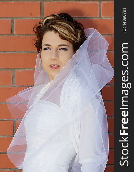 Young beautiful smiling woman, bride, standing near wall of red brick, outdoor shot. Young beautiful smiling woman, bride, standing near wall of red brick, outdoor shot