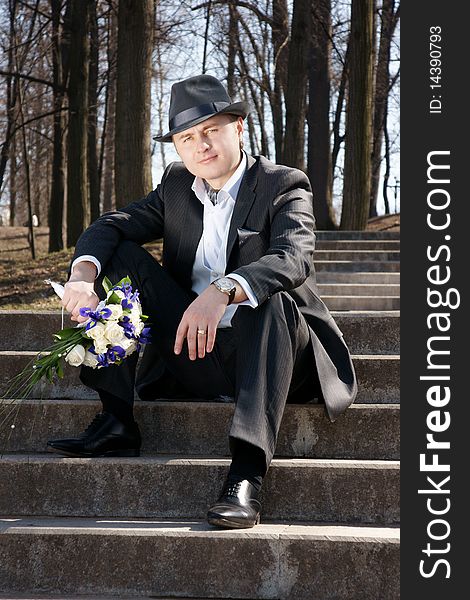 Young attractive smiling man, bridegroom, siting on stairs with bouquet, outdoor shot. Young attractive smiling man, bridegroom, siting on stairs with bouquet, outdoor shot